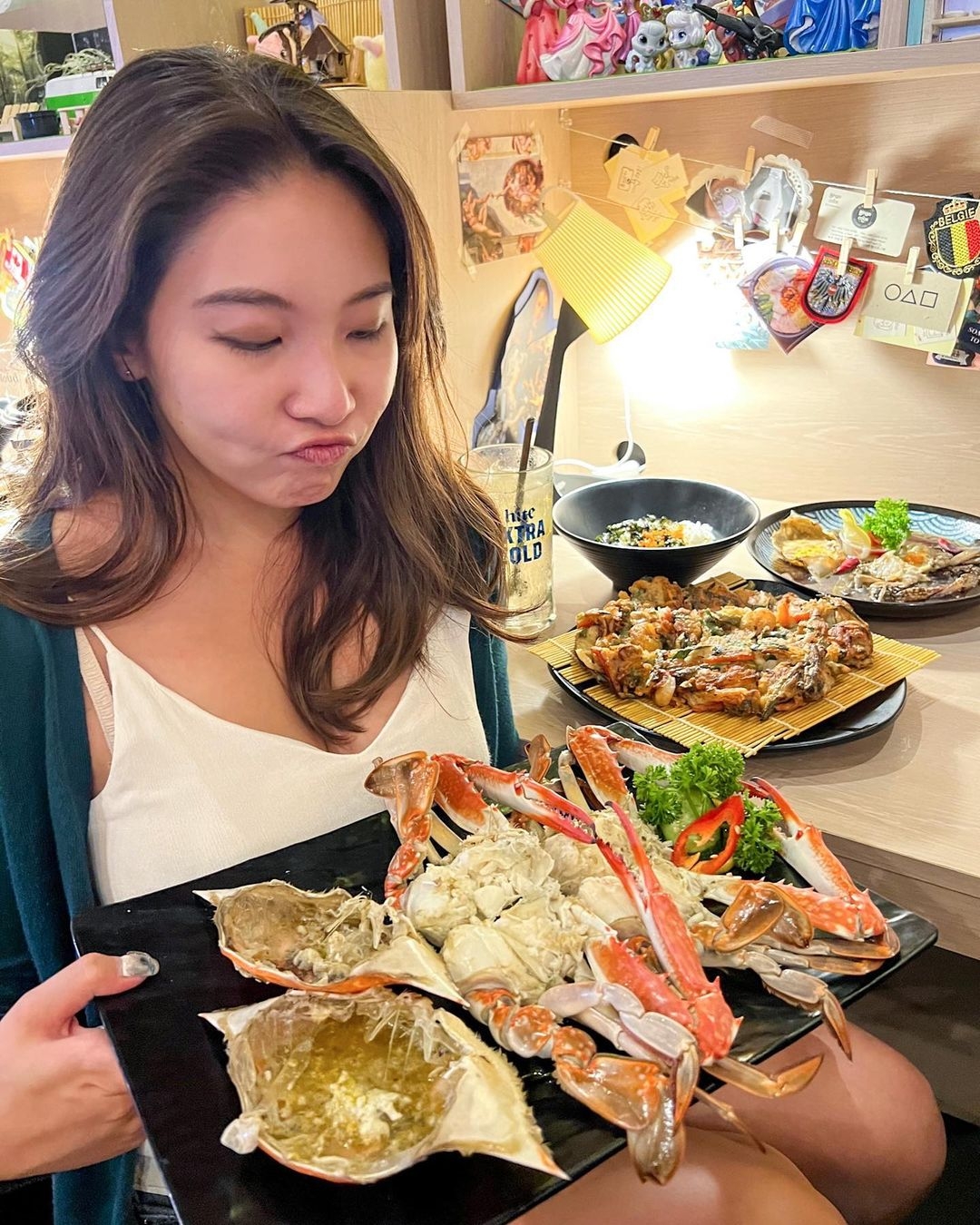 年輕女孩對著店裡的招牌螃蟹拍照，牆上的吊飾和照片充滿濃濃韓國元素。