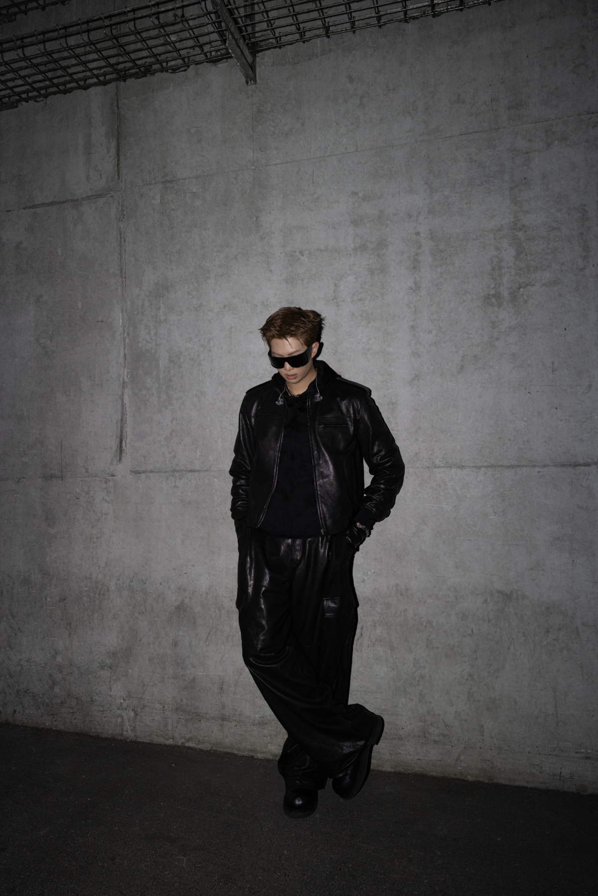 BTS 成員 RM 穿著一款 GUCCI 特別訂製的黑色皮革飛行夾克搭配工裝褲、手套、黑色絲綢黑色絲質針織連帽上衣、GUCCI 太陽眼鏡與手鍊。 