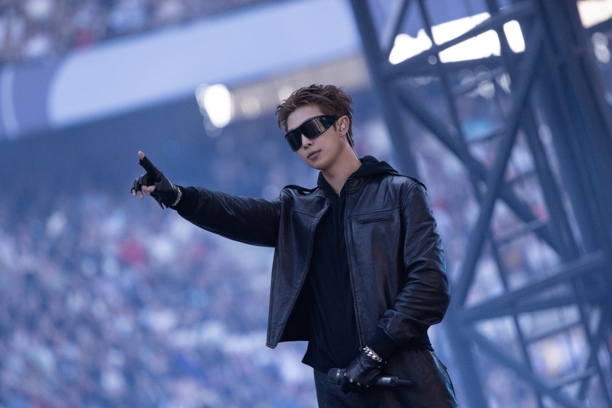 BTS 成員 RM 穿著一款 GUCCI 特別訂製的黑色皮革飛行夾克搭配工裝褲、手套、黑色絲綢黑色絲質針織連帽上衣、GUCCI 太陽眼鏡與手鍊。 