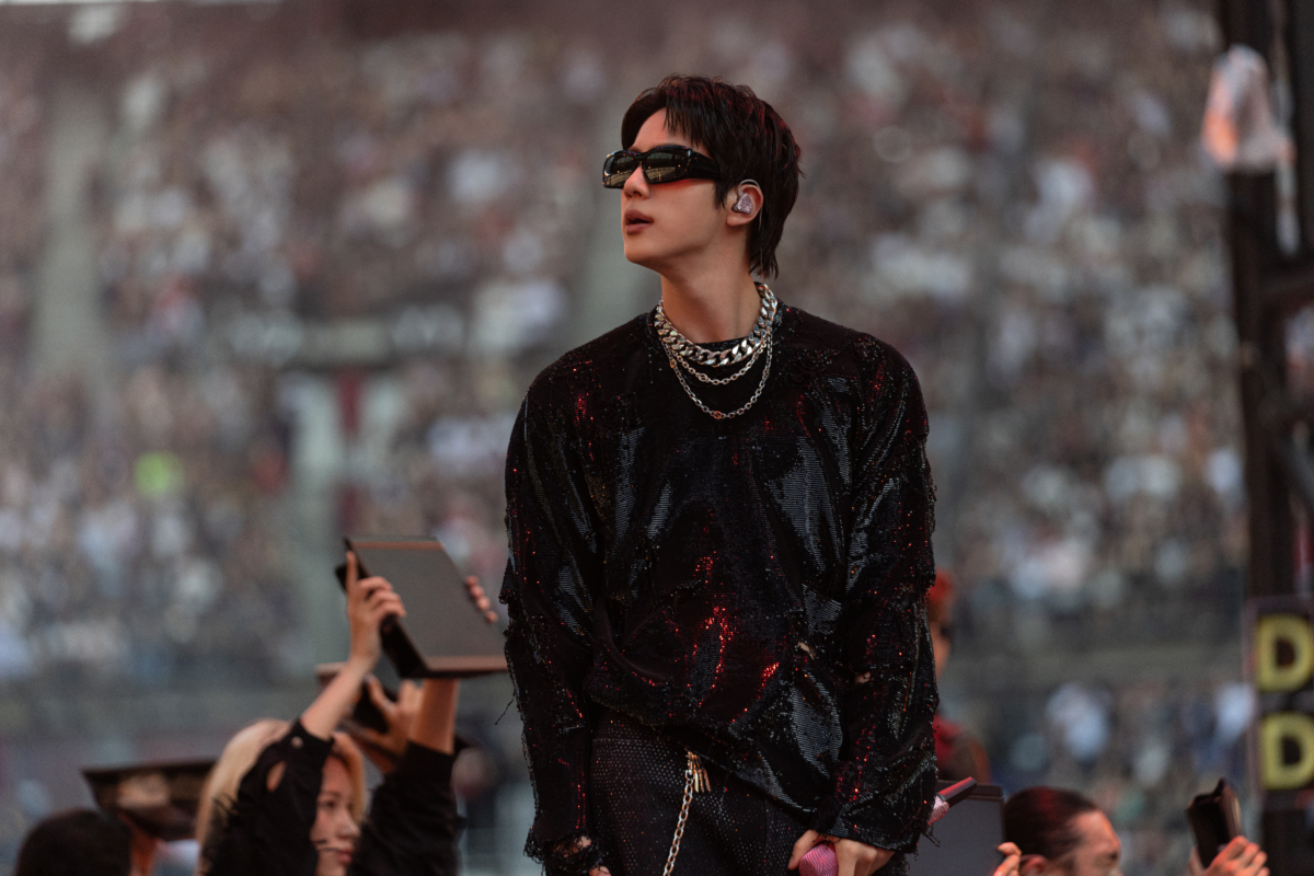 BTS 成員 Jin 穿著一款 GUCCI 特別訂製的黑色亮片刺繡長袖 T 恤，搭配綴滿水晶的黑色丹寧長褲、GUCCI 珠寶飾品與太陽眼鏡。 